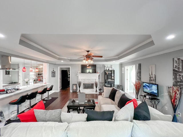 living room with a raised ceiling, crown molding, a high end fireplace, and wood-type flooring