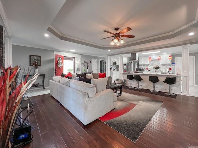 living room with ceiling fan, crown molding, dark wood-type flooring, and a tray ceiling