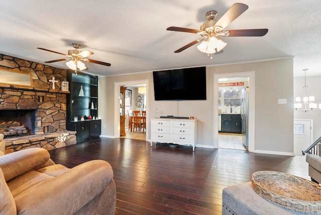 living room with ceiling fan with notable chandelier, dark hardwood / wood-style floors, a stone fireplace, and crown molding