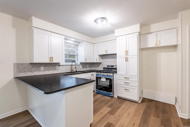 kitchen featuring sink, stainless steel stove, light hardwood / wood-style flooring, decorative backsplash, and white cabinetry