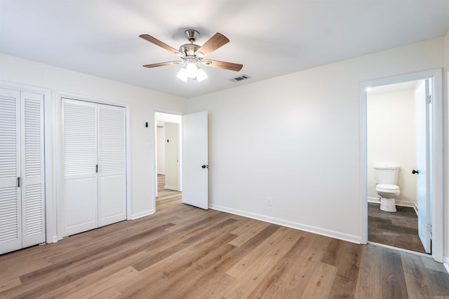 unfurnished bedroom featuring light wood-type flooring, two closets, ensuite bath, and ceiling fan