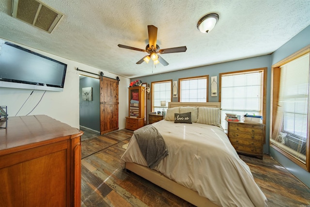 bedroom featuring dark hardwood / wood-style flooring, a barn door, a textured ceiling, and ceiling fan