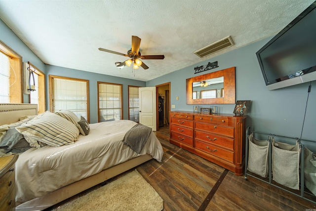 bedroom with multiple windows, ceiling fan, dark wood-type flooring, and a textured ceiling