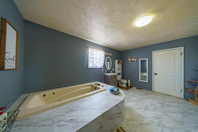 bathroom with vanity, toilet, a textured ceiling, and tiled bath