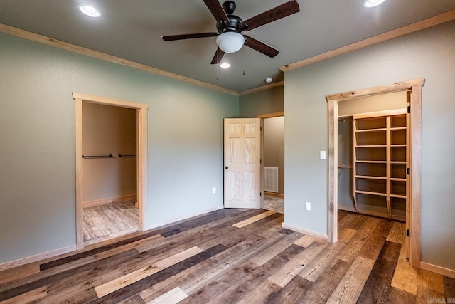 unfurnished bedroom with a spacious closet, ceiling fan, crown molding, a closet, and hardwood / wood-style flooring