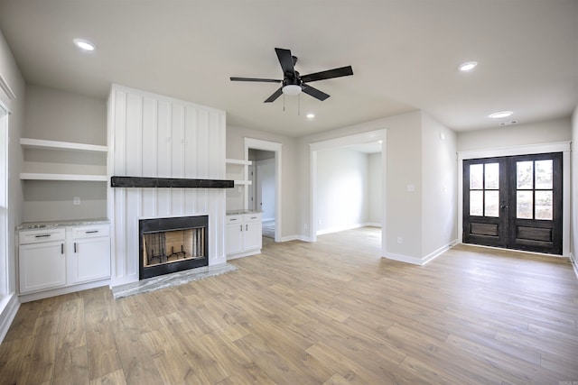 unfurnished living room featuring french doors, a large fireplace, light hardwood / wood-style flooring, and ceiling fan