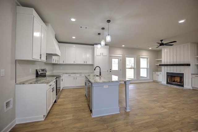 kitchen featuring stainless steel appliances, sink, white cabinets, light hardwood / wood-style floors, and an island with sink