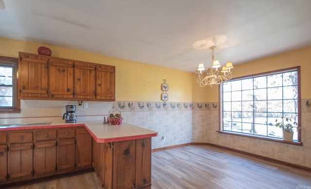 kitchen with kitchen peninsula, light hardwood / wood-style flooring, decorative light fixtures, and a notable chandelier