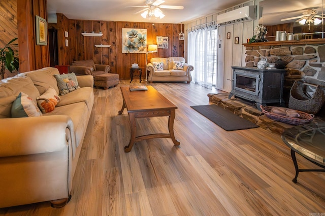 living room featuring light hardwood / wood-style floors, a wood stove, wooden walls, and a wall unit AC