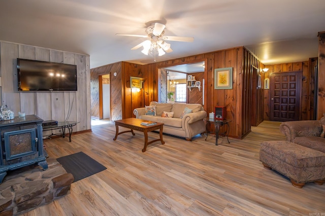 living room with light wood-type flooring, a wood stove, ceiling fan, and wood walls