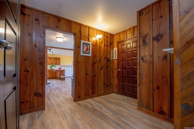 corridor with light wood-type flooring and wooden walls