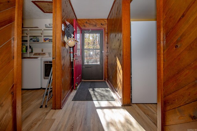 entryway with washing machine and clothes dryer, wood walls, light hardwood / wood-style floors, and a textured ceiling