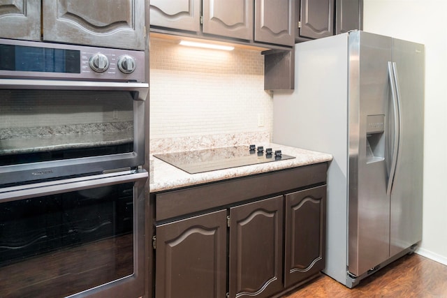 kitchen with dark brown cabinetry, decorative backsplash, appliances with stainless steel finishes, and hardwood / wood-style flooring