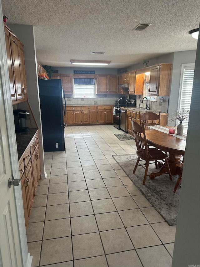 kitchen with a textured ceiling, sink, black fridge, stainless steel electric stove, and light tile patterned flooring