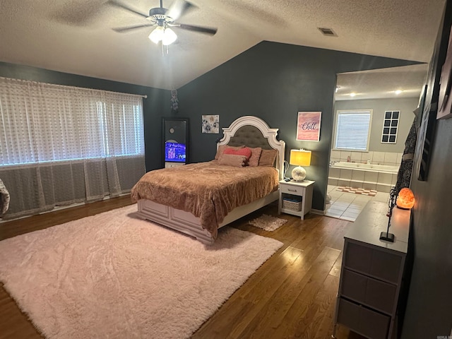 bedroom with ceiling fan, hardwood / wood-style flooring, a textured ceiling, connected bathroom, and lofted ceiling