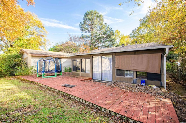 rear view of house with a trampoline, a sunroom, and a deck