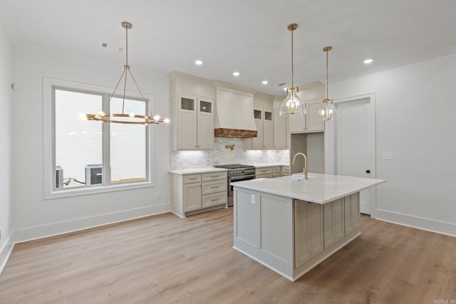 kitchen with high end range, a kitchen island with sink, light wood-type flooring, decorative light fixtures, and custom range hood