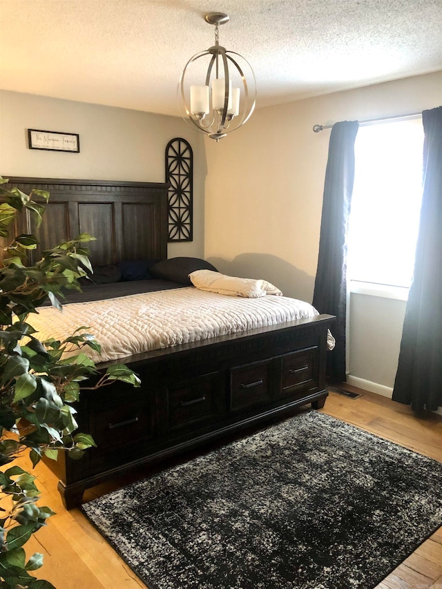 bedroom featuring light hardwood / wood-style flooring, a textured ceiling, and a notable chandelier