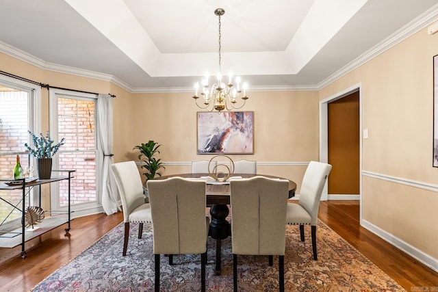 dining area featuring ornamental molding, dark hardwood / wood-style flooring, a raised ceiling, and a notable chandelier