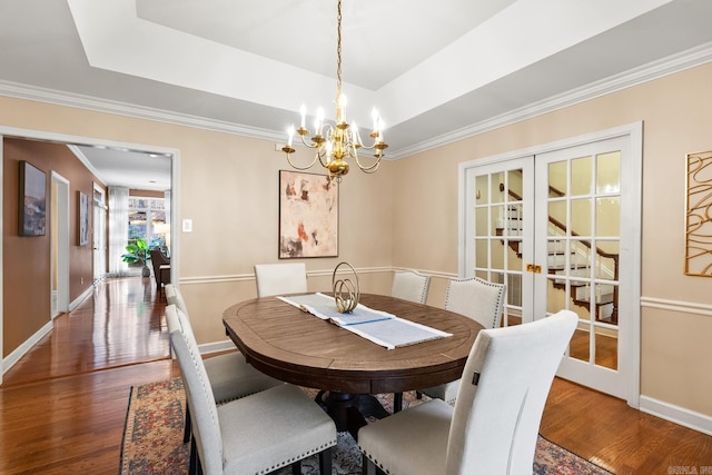 dining area featuring french doors, dark hardwood / wood-style flooring, an inviting chandelier, and a raised ceiling