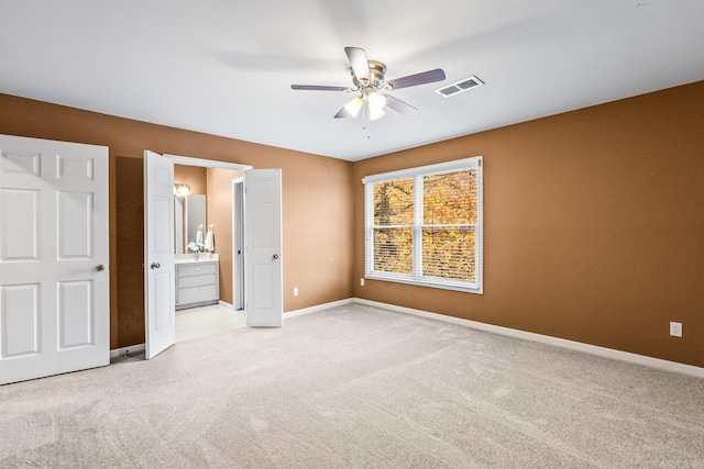 unfurnished bedroom with ceiling fan, ensuite bathroom, and light carpet