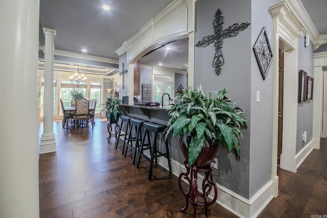 kitchen featuring dark hardwood / wood-style floors, ornamental molding, a breakfast bar, and decorative columns