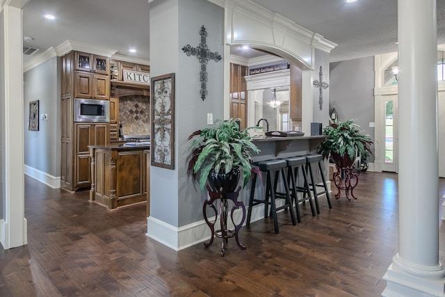 kitchen featuring kitchen peninsula, backsplash, ornate columns, dark hardwood / wood-style floors, and stainless steel microwave