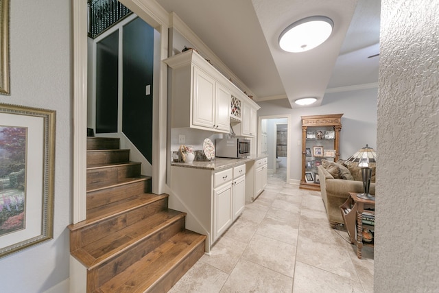 kitchen with white cabinets, light stone counters, light tile patterned floors, and crown molding