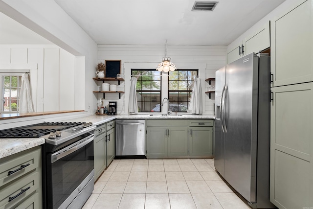 kitchen featuring hanging light fixtures, sink, wooden walls, light tile patterned floors, and stainless steel appliances