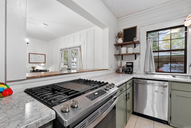 kitchen featuring appliances with stainless steel finishes, french doors, sink, wood walls, and light tile patterned flooring