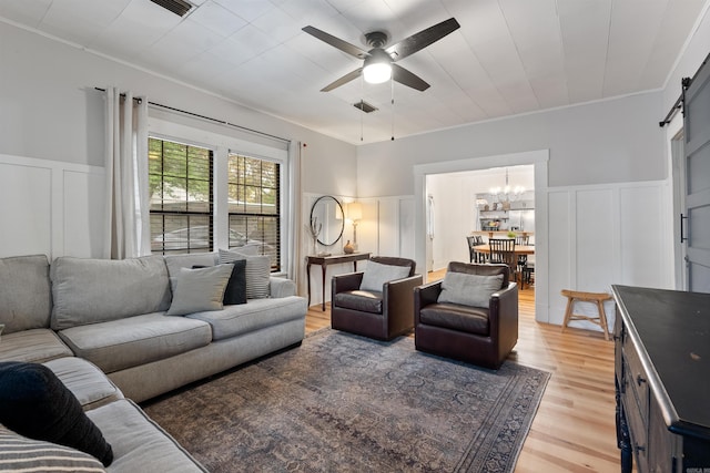 living room with ceiling fan with notable chandelier, a barn door, crown molding, and light hardwood / wood-style flooring