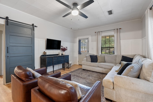 living room with a barn door, ceiling fan, crown molding, and light wood-type flooring