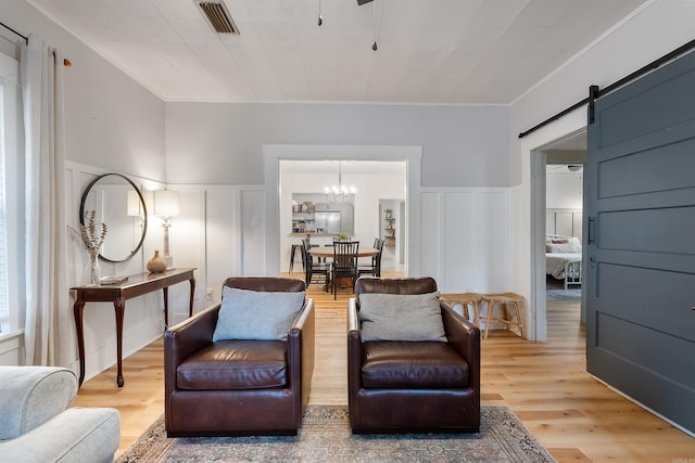 sitting room with a barn door, light hardwood / wood-style flooring, ornamental molding, and an inviting chandelier