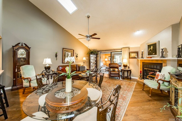 dining area with a skylight, high vaulted ceiling, light hardwood / wood-style flooring, and ceiling fan