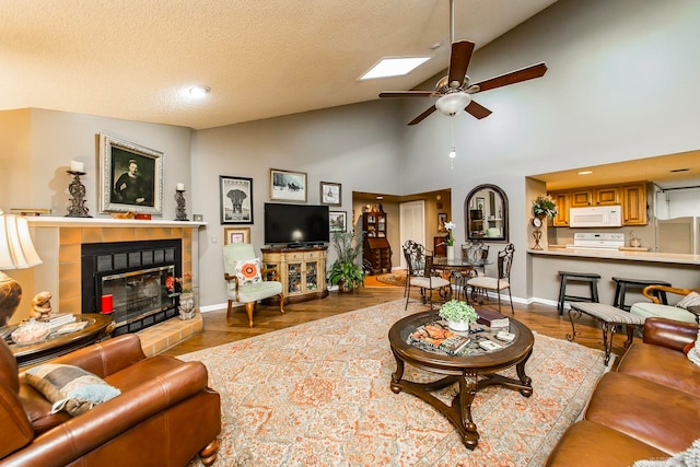 living room with a tile fireplace, ceiling fan, high vaulted ceiling, a textured ceiling, and light wood-type flooring