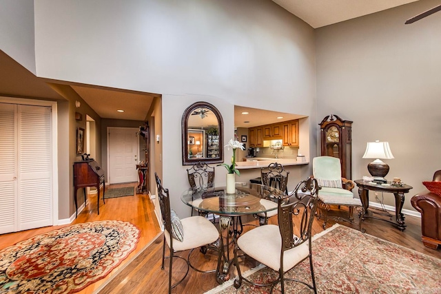 dining room with ceiling fan, light wood-type flooring, and a high ceiling