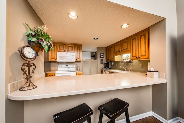 kitchen featuring a breakfast bar, white appliances, dark wood-type flooring, a textured ceiling, and kitchen peninsula