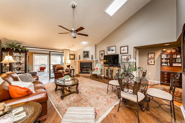 living room with a skylight, ceiling fan, high vaulted ceiling, and light wood-type flooring