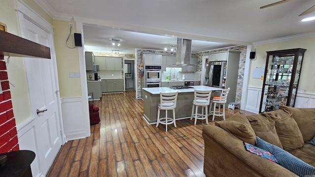 kitchen featuring appliances with stainless steel finishes, backsplash, a kitchen bar, dark hardwood / wood-style flooring, and island exhaust hood