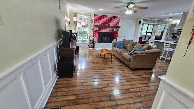 living room featuring a brick fireplace, ornamental molding, dark hardwood / wood-style floors, and ceiling fan