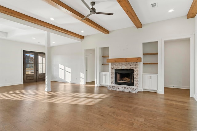 unfurnished living room with french doors, a brick fireplace, ceiling fan, dark wood-type flooring, and beam ceiling