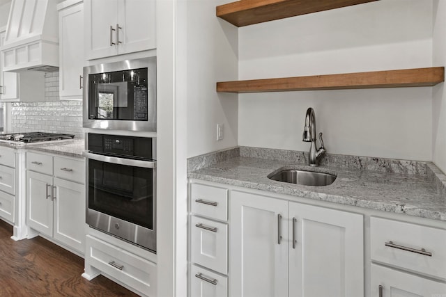 kitchen featuring appliances with stainless steel finishes, premium range hood, dark wood-type flooring, sink, and white cabinetry