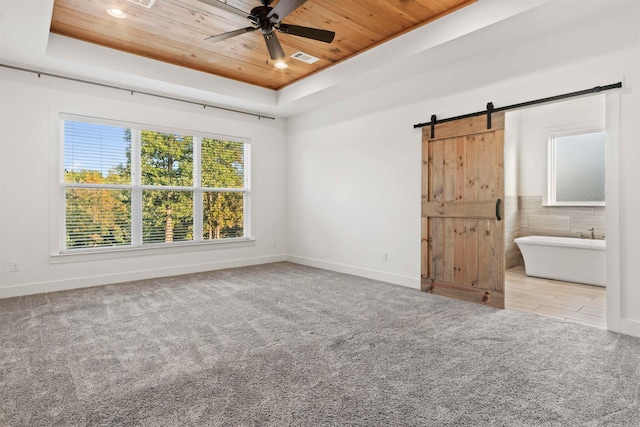 unfurnished room featuring a tray ceiling, a barn door, and light colored carpet