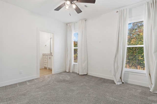 unfurnished bedroom with connected bathroom, light colored carpet, multiple windows, and ceiling fan