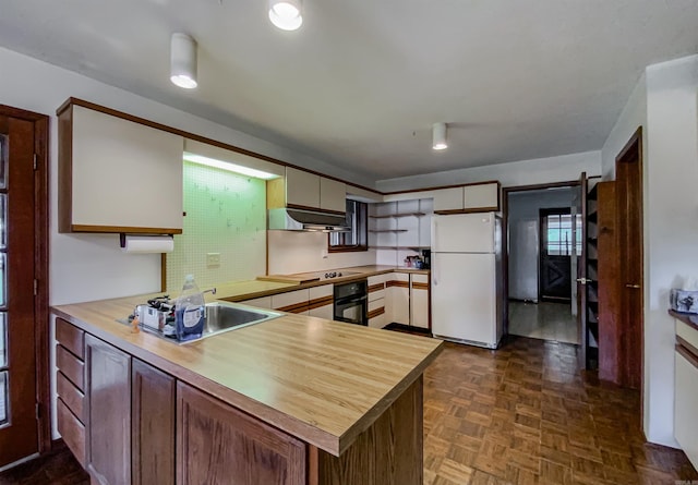 kitchen featuring kitchen peninsula, cooktop, ventilation hood, white refrigerator, and black oven