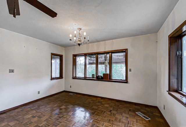 empty room featuring dark parquet flooring and a notable chandelier