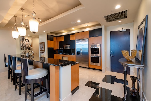 kitchen featuring kitchen peninsula, decorative light fixtures, a tray ceiling, a breakfast bar, and appliances with stainless steel finishes