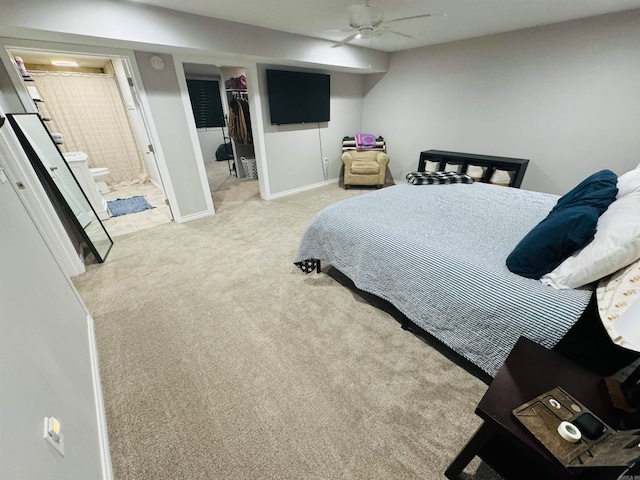 bedroom with a walk in closet, connected bathroom, light colored carpet, and ceiling fan