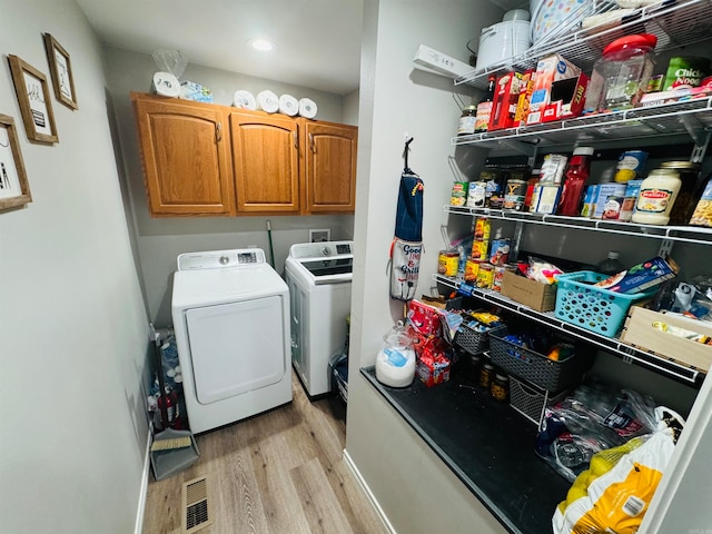 laundry area featuring washer and clothes dryer, light hardwood / wood-style floors, and cabinets