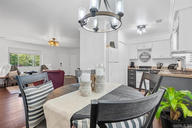 dining room with sink, dark hardwood / wood-style flooring, crown molding, and a notable chandelier